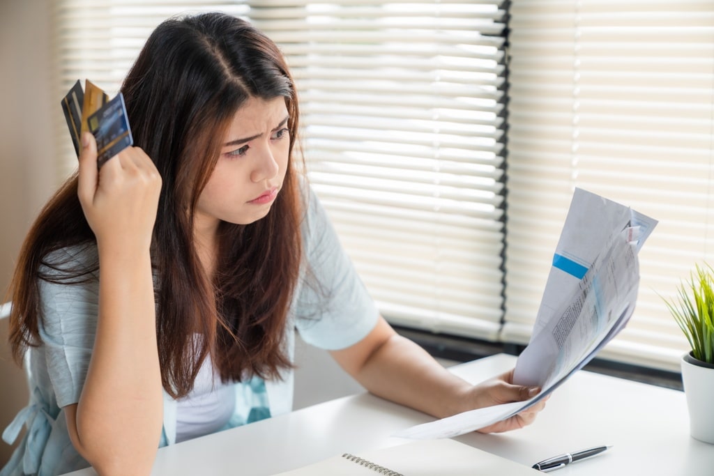 A stressed young woman looking at bills in one hand and holding multiple credit cards in the other referring to the stress of having multiple credit cards to pay for.