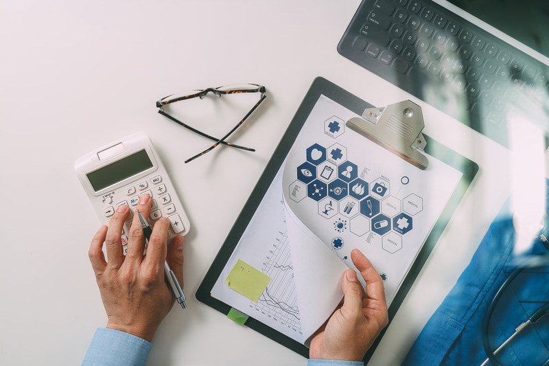 Male hands typing on a calculator while referring to a page filled with icons and a graph, indicating a medical loan concept