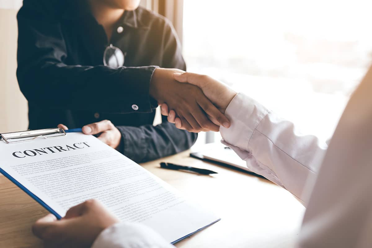 Two people shaking hands over a document titled ‘Contract’