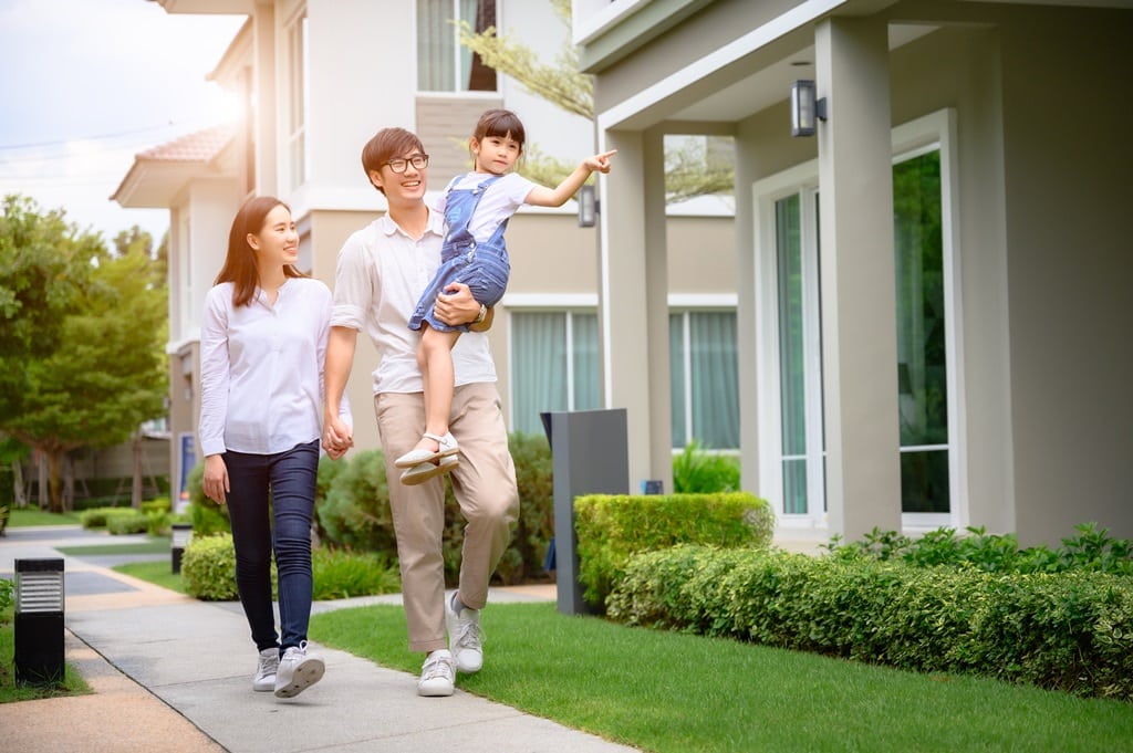 A couple with a young daughter walking beside houses happily to represent owning an asset such as a house