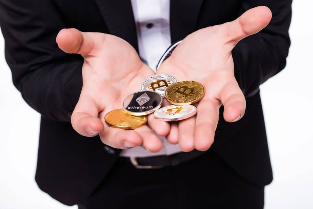 A suited man displaying different types of crypto coins in his hands