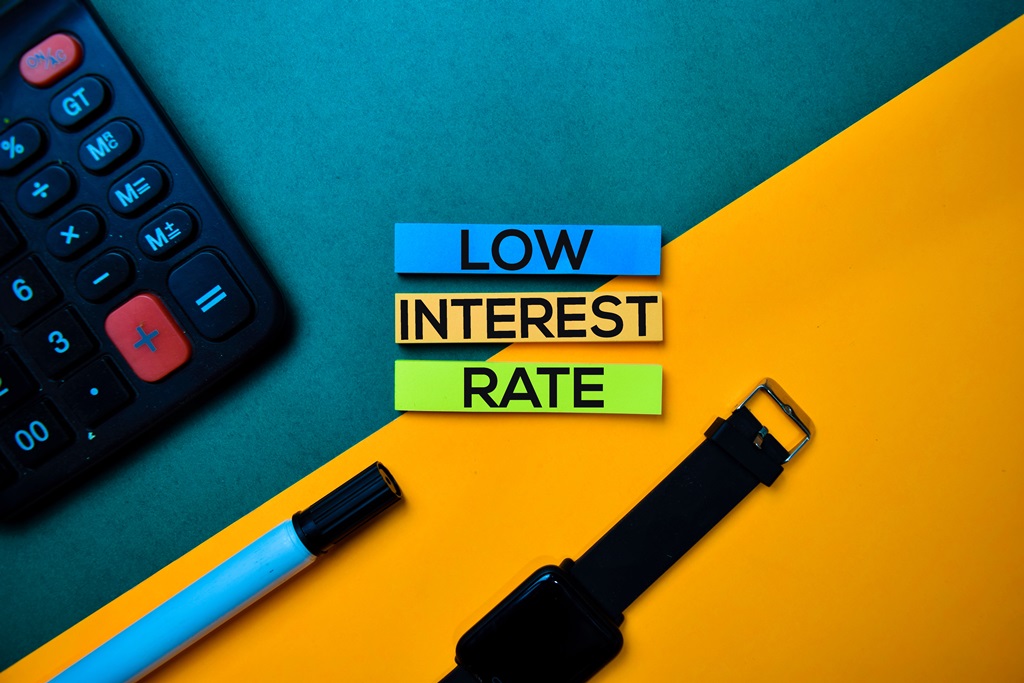 A background with a calculator, pen, and watch with the words ‘low interest rate’ printed in the centre referring to loans available at a low rate of interest