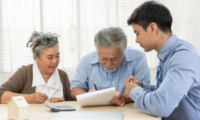Senior Asian couple signing medical loan document with young loan officer guiding them
